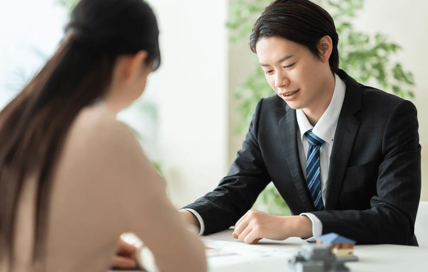 スーツ姿の担当者が、来店した女性に賃貸物件の資料を見せながら丁寧に説明している相談シーン。物件選びの打ち合わせを表す写真。